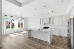Kitchen with stainless steel appliances, white cabinetry, glass fronted cabinets, a center island with sink, and decorative light fixtures