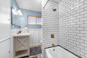 Full bath featuring vanity, a wainscoted wall, tub / shower combination, and a decorative wall
