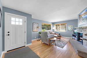 Living area with light wood-style flooring, a stone fireplace, and a textured ceiling