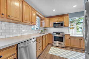 Kitchen with stainless steel appliances, recessed lighting, light wood-style floors, tasteful backsplash, and light stone countertops