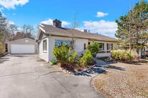 Single story home with a garage, an outdoor structure, a chimney, and roof with shingles