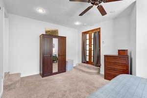 Bedroom with light carpet, ceiling fan, and a textured ceiling