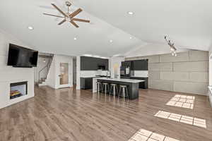 Kitchen with dark cabinetry, an island with sink, a breakfast bar, a ceiling fan, and open floor plan