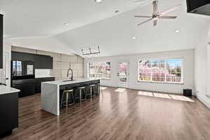 Two tone kitchen featuring freestanding refrigerator, a center island with sink, a kitchen bar, light stone countertops, and dark wood-style flooring