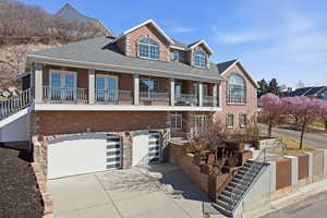 View of front facade featuring concrete driveway, a garage, roof with shingles, brick siding, and a balcony
