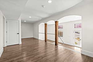 Spare room featuring arched walkways, decorative columns, dark wood finished floors, and recessed lighting