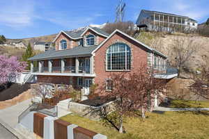 View of front of property featuring brick siding, a balcony, a garage, concrete driveway, and a front yard