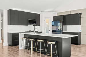 Kitchen with modern cabinets, dark cabinets, an island with sink, light wood-style flooring, and lofted ceiling