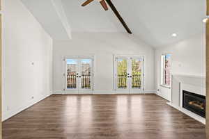 Unfurnished living room featuring french doors, a glass covered fireplace, dark wood-style floors, a ceiling fan, and vaulted ceiling