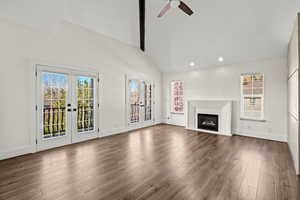 Unfurnished living room featuring french doors, dark wood-style floors, a ceiling fan, a glass covered fireplace, and vaulted ceiling