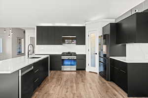 Kitchen with modern cabinets, dark cabinetry, stainless steel range with gas cooktop, and light wood-type flooring
