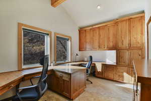 Home office featuring built in desk, light carpet, and lofted ceiling with beams