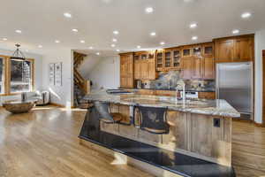 Kitchen featuring dark stone counters, stainless steel appliances, wood finish cabinetry, glass fronted cabinets, and light wood finished floors