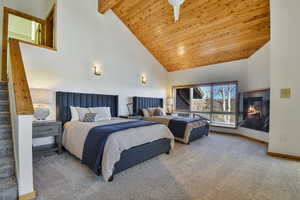 Bedroom with a vaulted wood ceiling, carpet flooring, a ceiling fan, and a glass covered fireplace