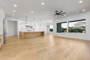 Kitchen featuring open floor plan, hanging lights, a large island, a ceiling fan, and light wood finished floors