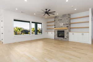 Unfurnished living room featuring a ceiling fan, a stone fireplace, light wood finished floors, and recessed lighting