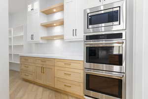 Kitchen with stainless steel appliances, light wood finished floors, backsplash, open shelves, and glass insert cabinets