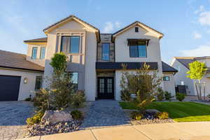 View of front facade with french doors, stucco siding, a front lawn, and driveway