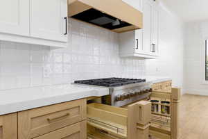 Kitchen with light wood-style floors, backsplash, stainless steel gas cooktop, and white cabinetry