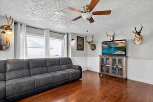 Living room featuring wood-type flooring, a ceiling fan, a textured ceiling, and a wainscoted wall
