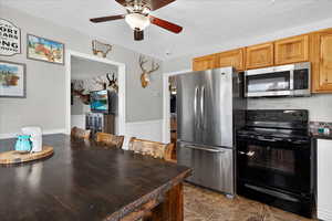 Kitchen with stainless steel appliances, a textured ceiling, a ceiling fan, and a wainscoted wall
