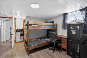 Bedroom with an office area, light wood-style floors, and a textured ceiling