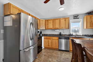 Kitchen featuring stainless steel appliances, dark countertops, ceiling fan, and a textured ceiling