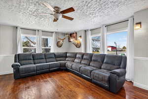 Living room featuring wainscoting, ceiling fan, hardwood / wood-style floors, a textured wall, and a textured ceiling