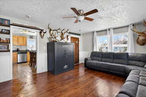 Living area featuring a ceiling fan, wainscoting, dark wood-style floors, and a textured ceiling