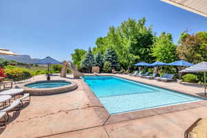 View of pool with a water slide, patio surround, and an in-ground hot tub