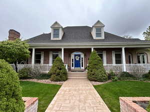 View of front of property featuring covered porch, brick siding, roof with shingles, and a front lawn