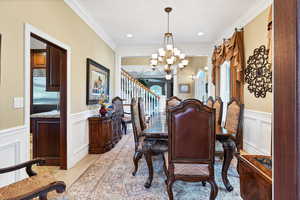 Dining area featuring ornamental molding, a wainscoted wall, a decorative wall, and suspended lighting
