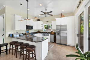 Kitchen with stainless steel appliances, a peninsula, a breakfast bar area, white cabinets, and dark stone counters