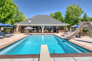 View of pool featuring a water slide, patio surround, a diving board, and a bar