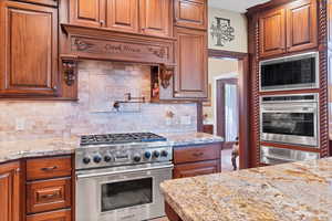 Kitchen with stainless steel appliances, a warming drawer, light stone countertops, wood finish cabinets, and backsplash