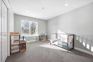 Carpeted bedroom with a crib, recessed lighting, and a closet