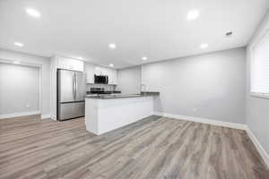 Kitchen with a peninsula, stainless steel appliances, white cabinets, light wood finished floors, and recessed lighting