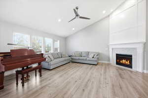 Living room with lofted ceiling, light wood-style flooring, a ceiling fan, a fireplace, and recessed lighting