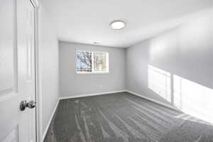 Spare room featuring dark colored carpet and baseboards