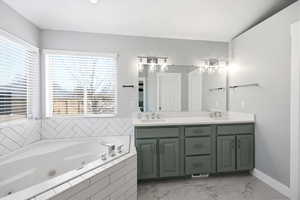 Full bath featuring double vanity, a whirlpool tub, and light marble finish flooring