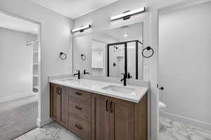 Bathroom with a spacious closet, double vanity, a shower stall, and light marble finish flooring