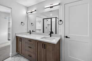 Full bath featuring a walk in closet, a stall shower, double vanity, and light marble finish flooring