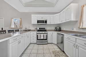 Kitchen with stainless steel appliances, white cabinets, lofted ceiling, light tile patterned flooring, and dark countertops