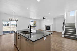 Kitchen with an island with sink, open floor plan, ceiling fan, a tile fireplace, and dark wood-type flooring