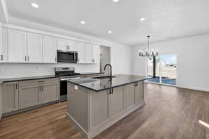 Two tone kitchen featuring stainless steel appliances, a kitchen island with sink, backsplash, dark wood-style flooring, and hanging lights