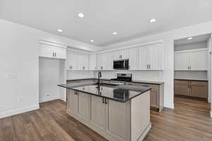 Kitchen with stainless steel appliances, a kitchen island with sink, dark wood-style floors, white cabinets, and recessed lighting