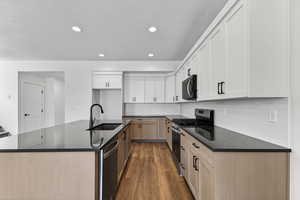 Dual tone kitchen with a center island with sink, two tone color scheme, stainless steel appliances, dark wood-style flooring, and dark stone counters