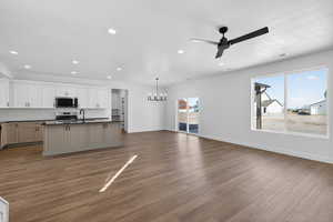 Kitchen with a kitchen island with sink, a chandelier, open floor plan, a ceiling fan, and dark wood-type flooring