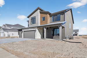 Contemporary house with a porch, concrete driveway, stone siding, a standing seam roof, and a garage