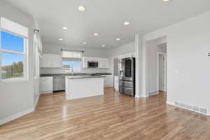 Kitchen featuring white cabinetry, stainless steel appliances, recessed lighting, a kitchen island, and light wood finished floors
